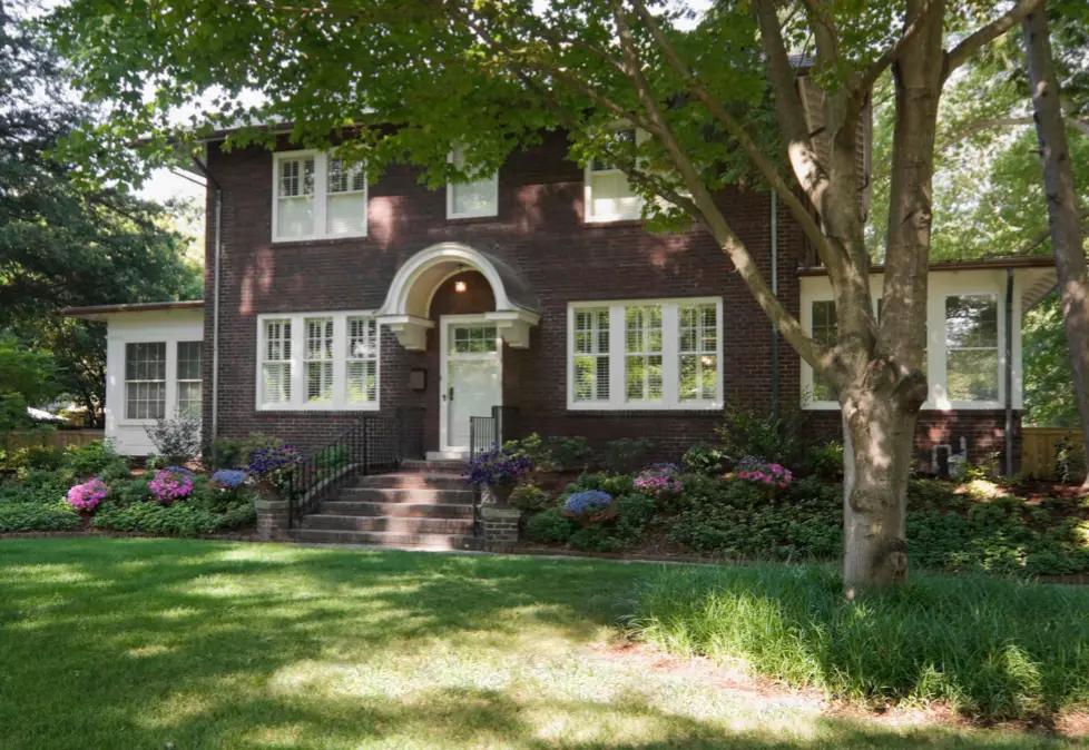 Happy homeowner holding keys in front of a new house, while their previous home is visible in the background.